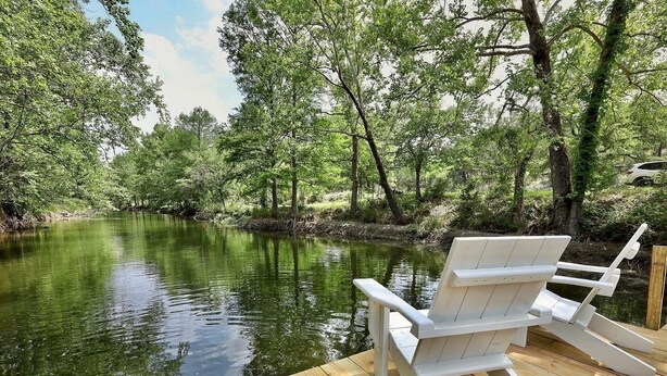 A wooden deck with a white Adirondack chair facing a calm river surrounded by lush greenery. - Secluded, Romantic Yurt w/Hot Tub at The Yurtopian - "Dottie" (Dripping springs)