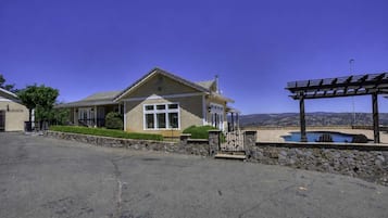 Uma casa térrea com um muro de pedra, um alpendre coberto e vista para uma paisagem montanhosa.