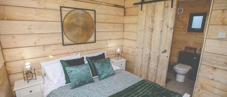 A wooden-paneled bedroom with a bed, two bedside tables, a framed artwork, and a sliding door leading to a bathroom.