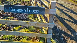 Ein Holzschild mit der Aufschrift 'Edgmond Lodges', umgeben von einem Holzzaun und einem Kiesweg.