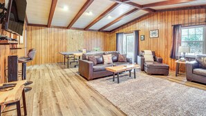 A cozy living room with wooden walls and ceiling, a brown leather sofa, a coffee table, and a TV mounted on the wall. - 4 Mi to Savannah: Home w/ Gazebo & Seasonal Pool! (Garden City)