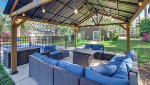 A covered outdoor seating area with wicker furniture and a pool in the background. - 4 Mi to Savannah: Home w/ Gazebo & Seasonal Pool! (Garden City)
