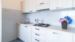 Et moderne køkken med hvide skabe, en gasblus, en vask og en vase med blomster på bordpladen.