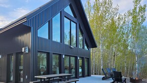 Een modern gebouw met grote ramen en een patio, inclusief een vuurkorf en zitplaatsen.