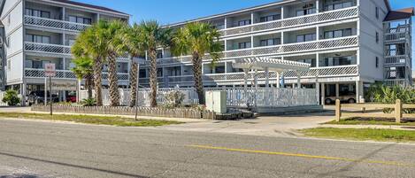 A multi-story hotel with balconies, palm trees, and a 'No Parking' sign.