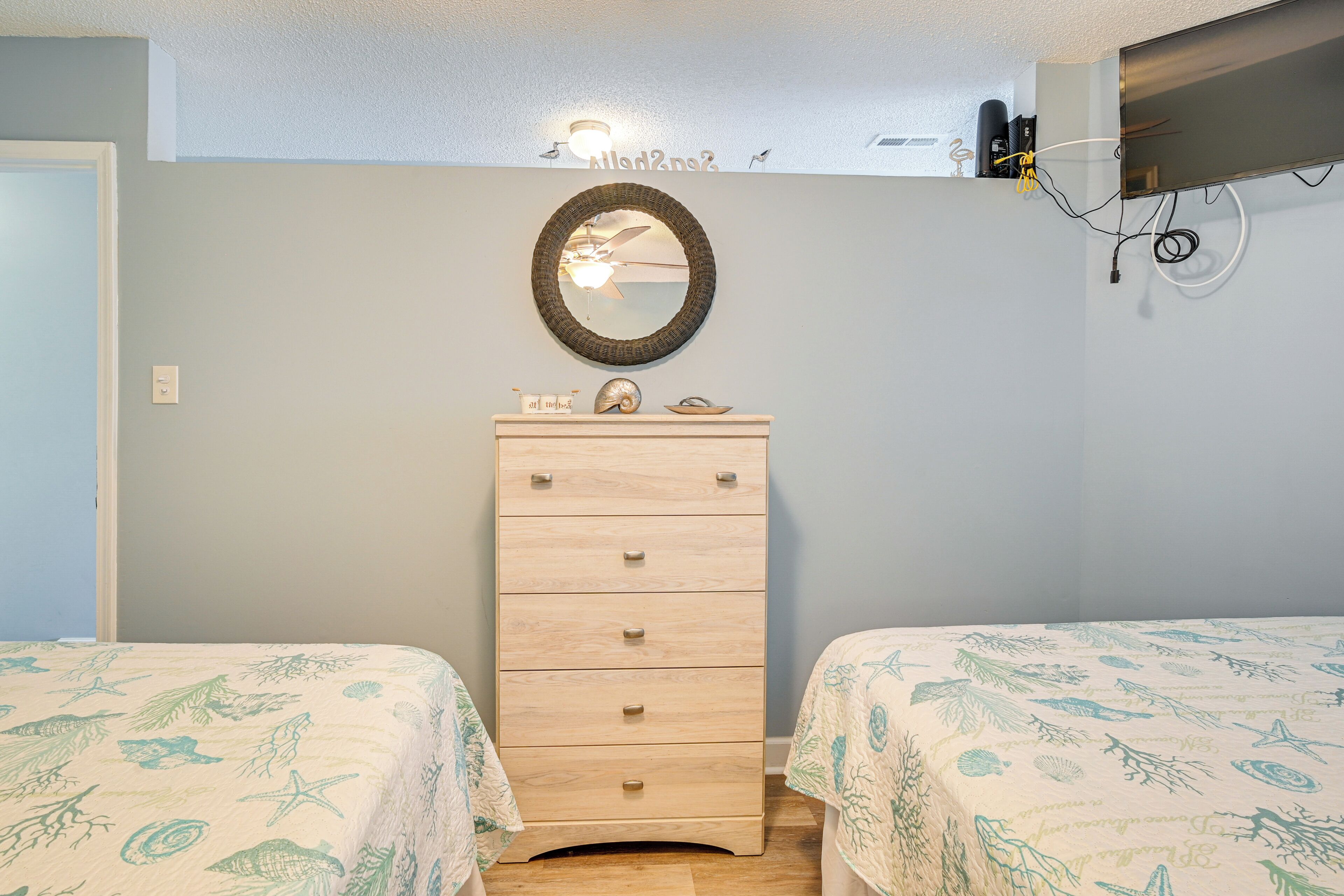 A bedroom with two beds, a dresser, a mirror, and a ceiling fan.