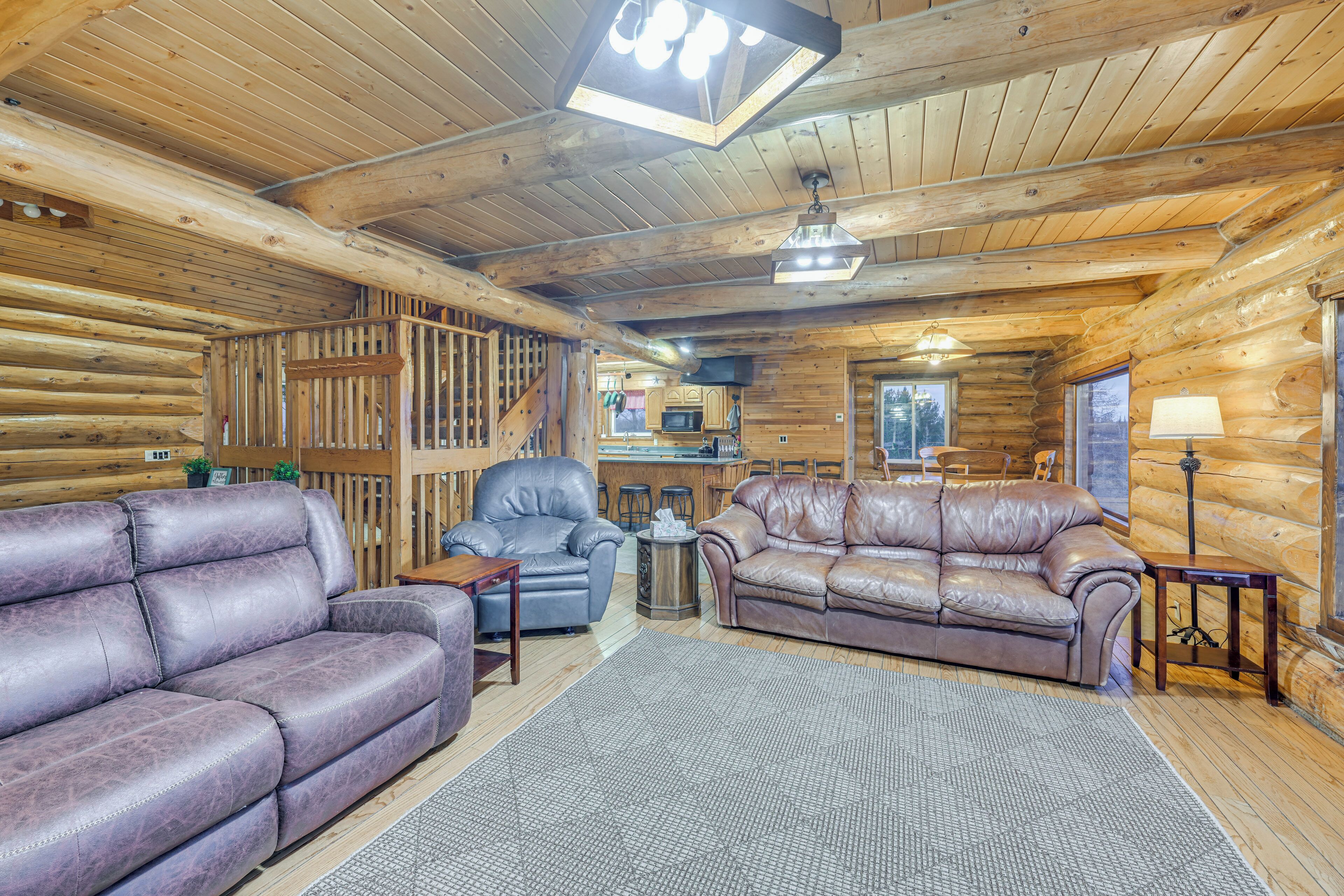 A log cabin interior with two leather sofas, a dining area, and a kitchen.