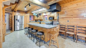 A wooden cabin interior with a kitchen featuring a stainless steel refrigerator, a microwave, and a large island with bar stools.
