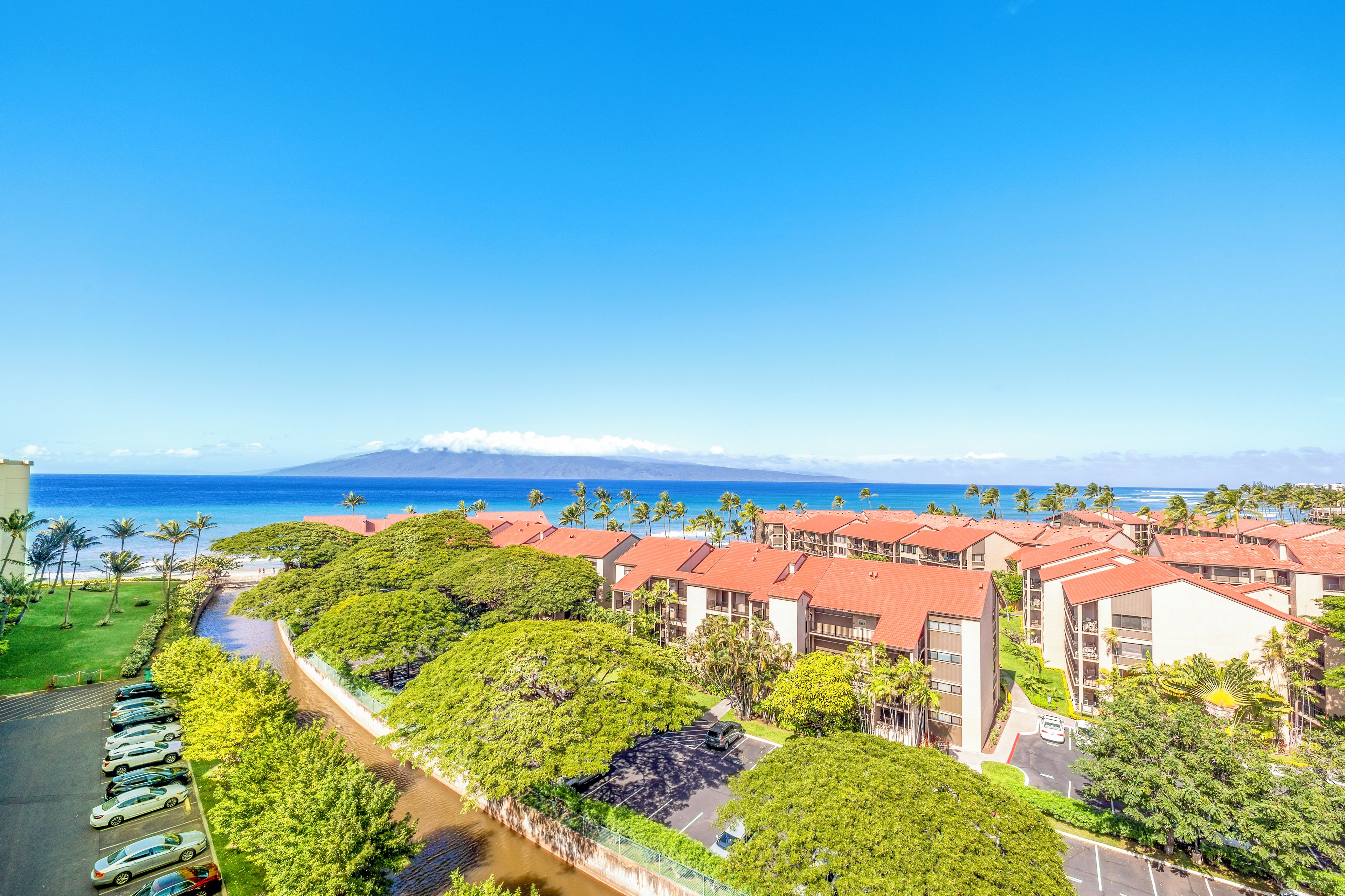 A resort with multiple buildings, a parking area, and a view of the ocean.
