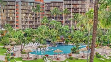 A hotel with multiple floors, outdoor swimming pool, and lush greenery.