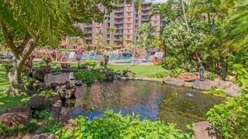 A hotel with a pool, lush greenery, and a small pond.