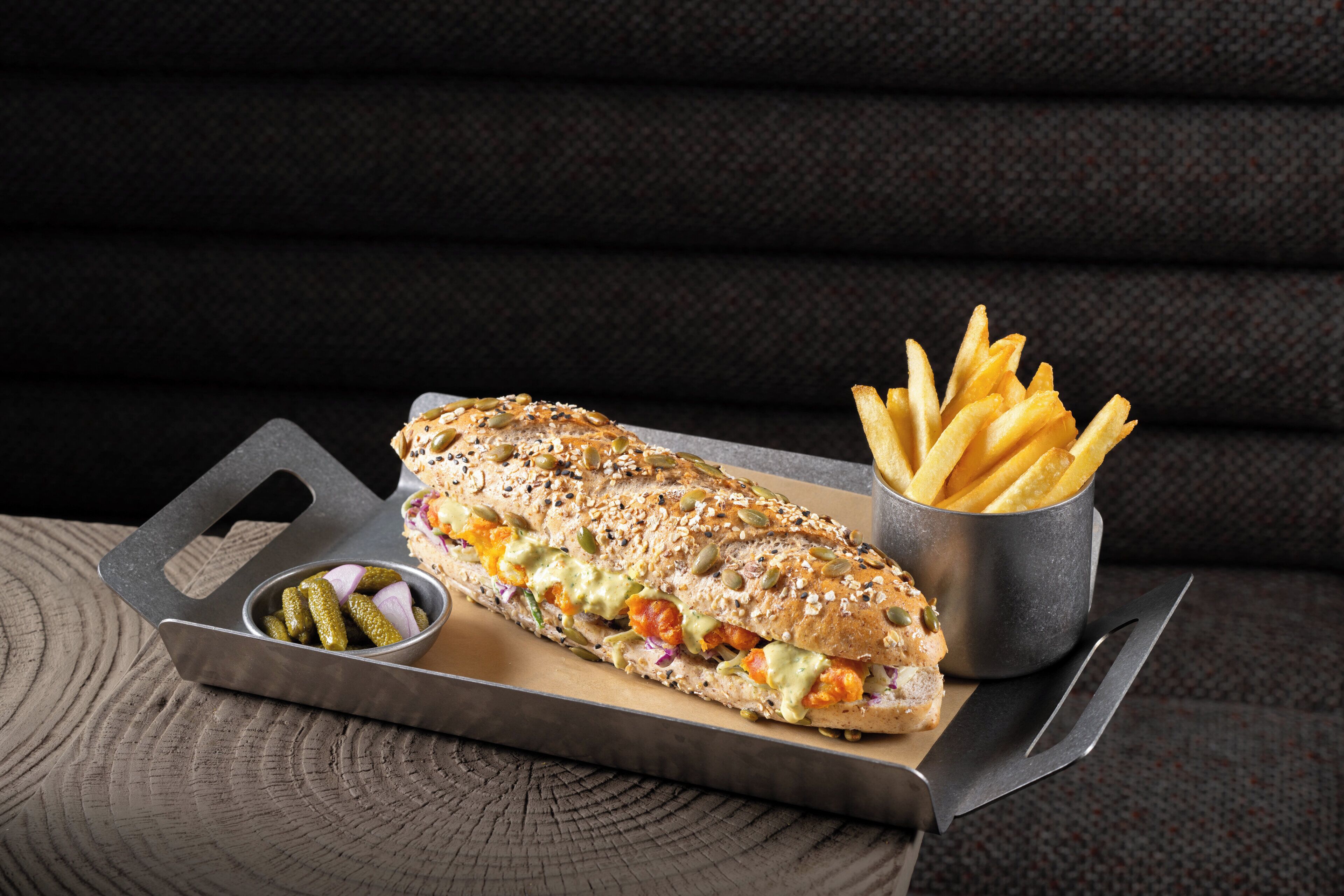 Un sandwich avec des cornichons et des frites, servi sur un plateau.
