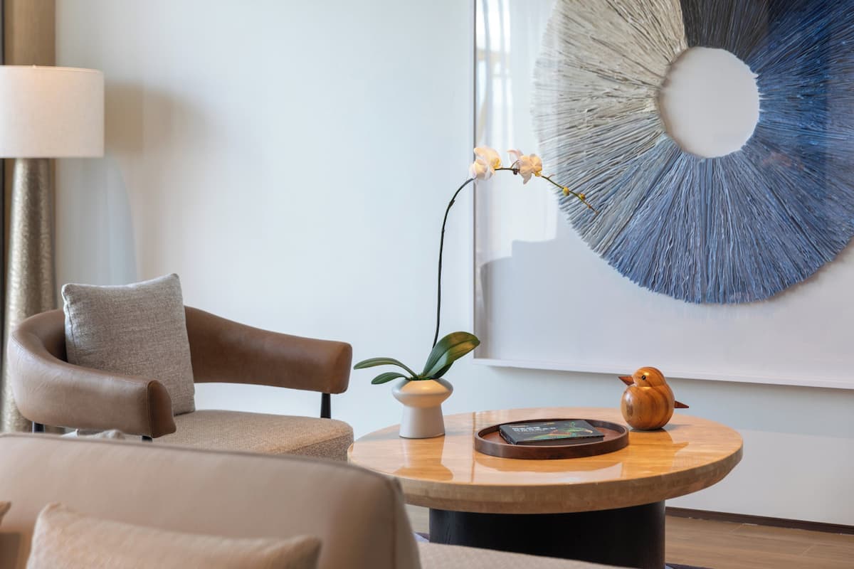 A modern living room with a leather armchair, a round wooden coffee table, a vase with orchids, and a wall art piece.