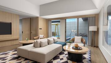 Ein modernes Hotelzimmer mit einer großen Couch, einem runden Couchtisch, einem an der Wand montierten Fernseher und einem Balkon mit Sitzgelegenheit.