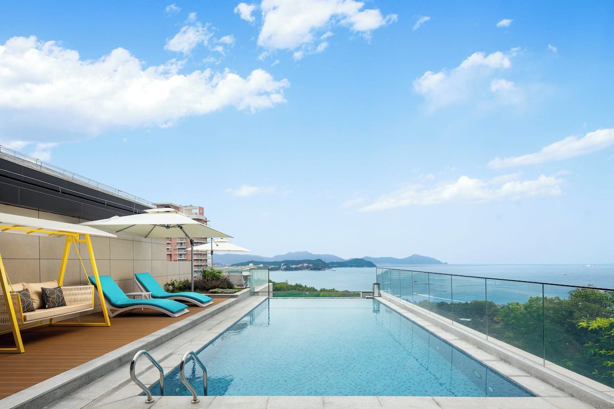 A poolside area with a swing chair, sun loungers, and a view of the sea.