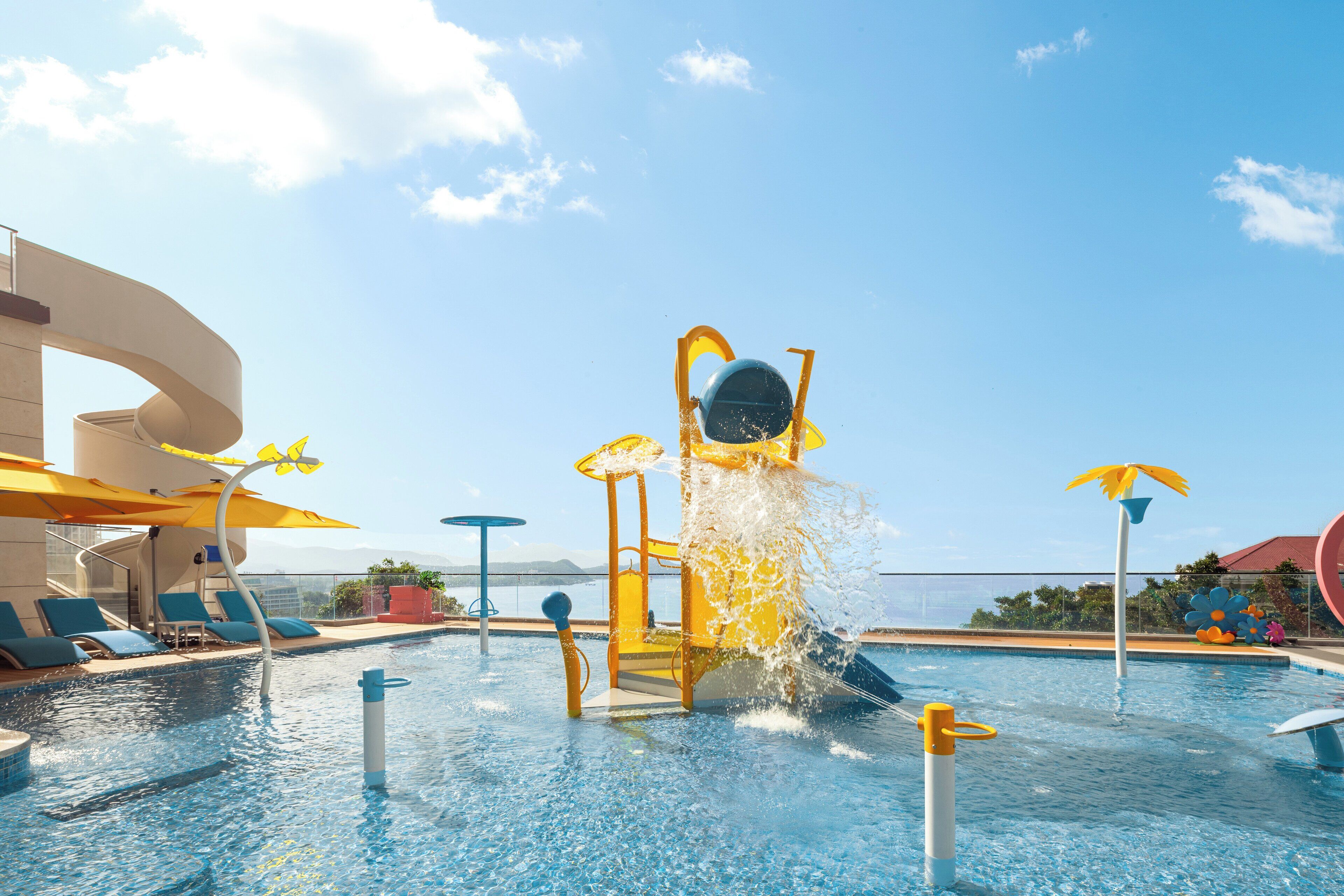 Un espace piscine équipé d’un toboggan, de chaises longues et d’un parasol.