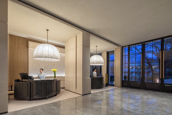Un espace d’accueil moderne doté de deux comptoirs de réception, de grands luminaires suspendus et offrant une vue sur l’extérieur grâce à de larges fenêtres.