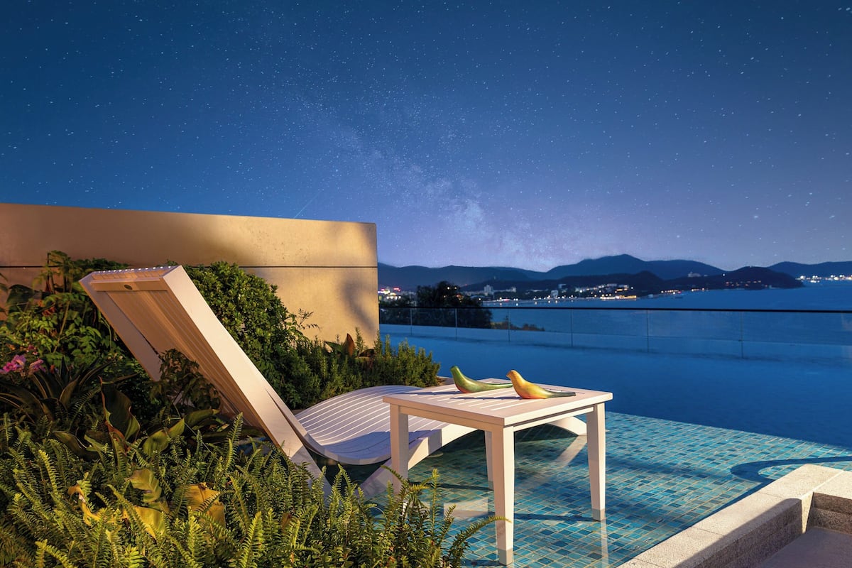 Relax in a serene poolside setting surrounded by lush greenery and a clear view of the night sky.