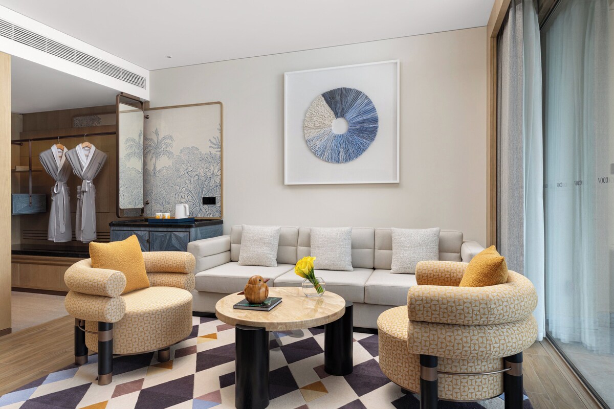 A modern living room with a sofa, two armchairs, a coffee table, and a large abstract painting.