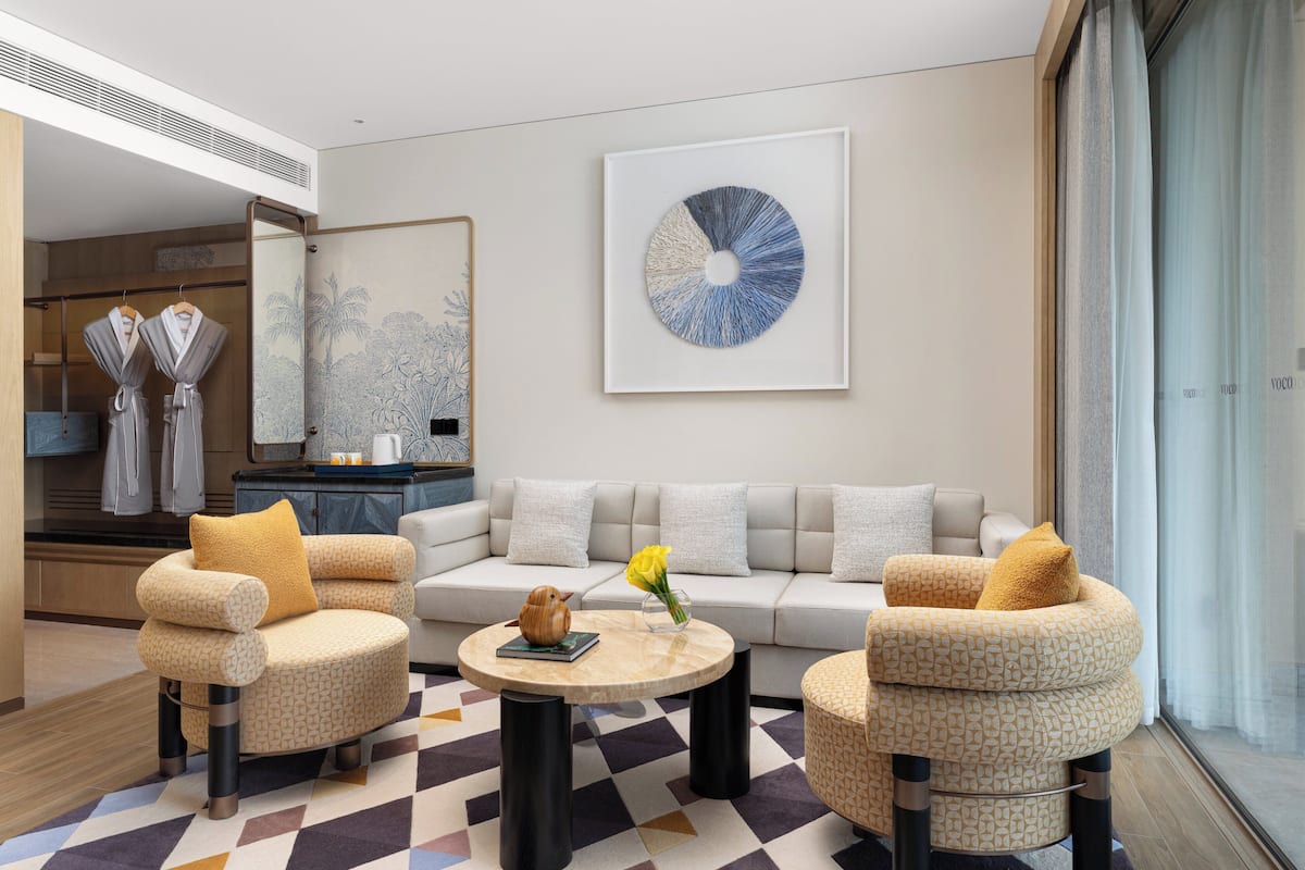 A modern living room with a sofa, two armchairs, a coffee table, and a large abstract painting.
