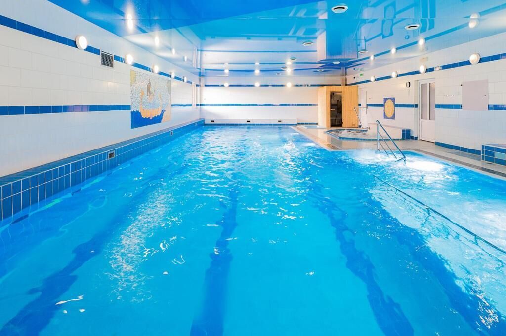Ein Hallenbad mit klarem, blauen Wasser, gefliesten Wänden und einer Decke mit Einbauten für Beleuchtung.