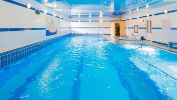 Ein Hallenbad mit klarem, blauen Wasser, gefliesten Wänden und einer Decke mit Einbauten für Beleuchtung.