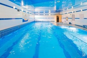 Una piscina interior con agua azul cristalina, paredes con azulejos e iluminación empotrada en el techo.