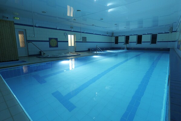 An indoor swimming pool with clear lanes, a starting block, and a lifeguard chair.