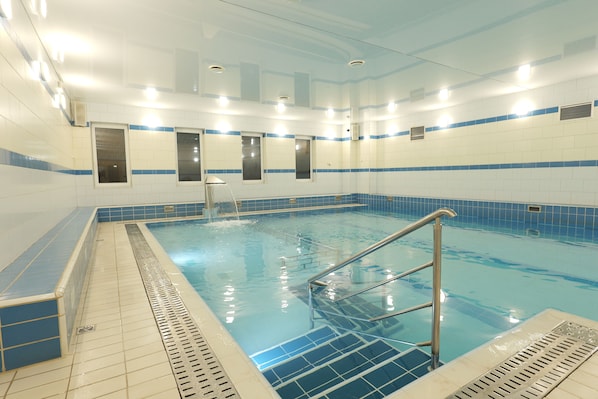 Una piscina interior con agua cristalina, paredes de azulejos y una escalera metálica.