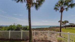 A coastal view with a white fence, palm trees, and a clear sky.