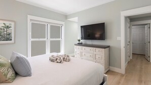 Un dormitorio con cama, televisor, ventilador de techo y una puerta que da a otra habitación.