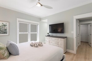 A bedroom with a bed, a television, a ceiling fan, and a door leading to another room.