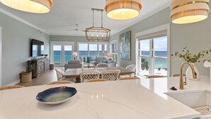 Una cocina moderna con una isla grande, iluminación colgante y vistas al océano.