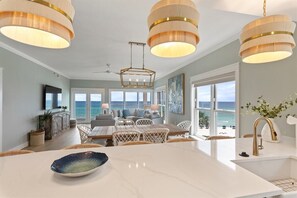 A modern kitchen with a large island, pendant lighting, and a view of the ocean.