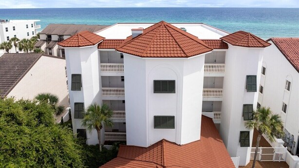 Un hotel de varios pisos con techo de tejas rojas, paredes blancas y balcones con vista a la playa.