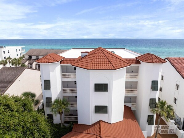 A multi-story hotel with a red-tiled roof, white walls, and balconies overlooking a beach.