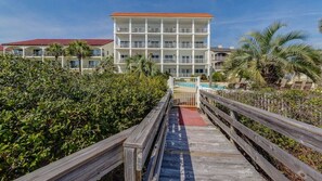 A multi-story hotel with a pool, surrounded by greenery and a wooden walkway.