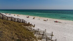 A beach with a wooden walkway leading to the shore, sandy beach, and clear blue water.