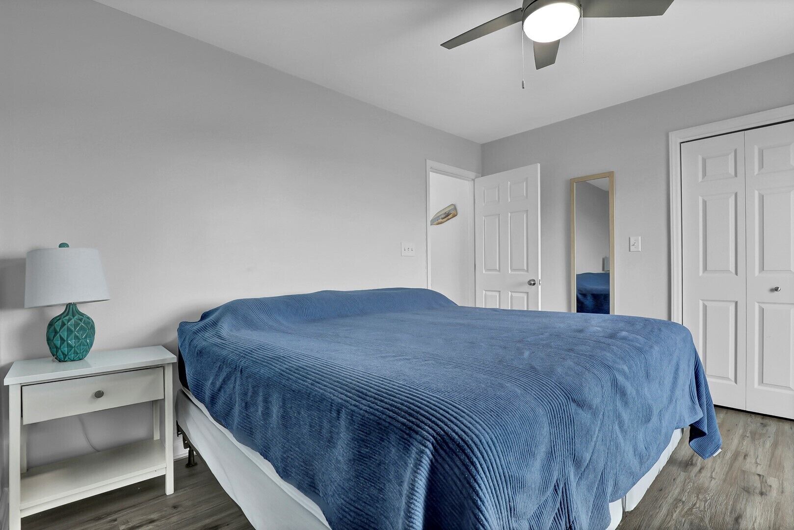 Un dormitorio con cama, mesita de noche, lámpara, ventilador de techo y puertas blancas.