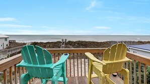 Une terrasse en bois avec deux fauteuils Adirondack donnant sur une plage.
