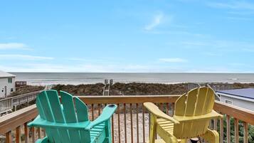 A wooden deck with two Adirondack chairs facing a beach.