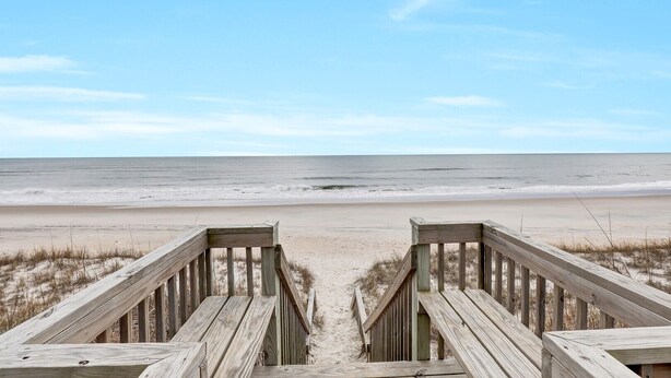 Une promenade en bois qui mène à une plage d’où l’on a une vue dégagée sur l’océan.