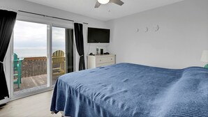 Une chambre avec un lit, un ventilateur de plafond, une télévision et une vue sur l’océan, accessible par une porte coulissante.