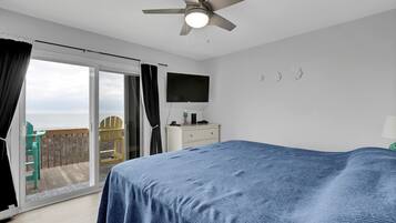 A bedroom with a bed, a ceiling fan, a TV, and a view of the ocean through a sliding door.