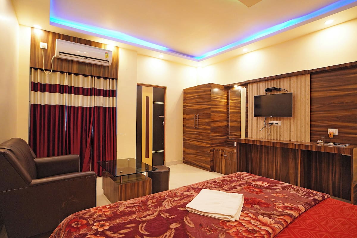 A hotel room with a bed, a desk, a chair, a TV, and an air conditioning unit.
