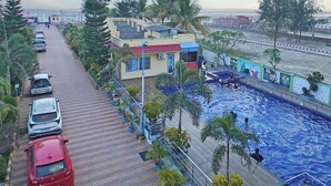 A swimming pool with a tiled deck, surrounded by palm trees and a few parked cars. - Marino Beach Resorts (Kanthi)