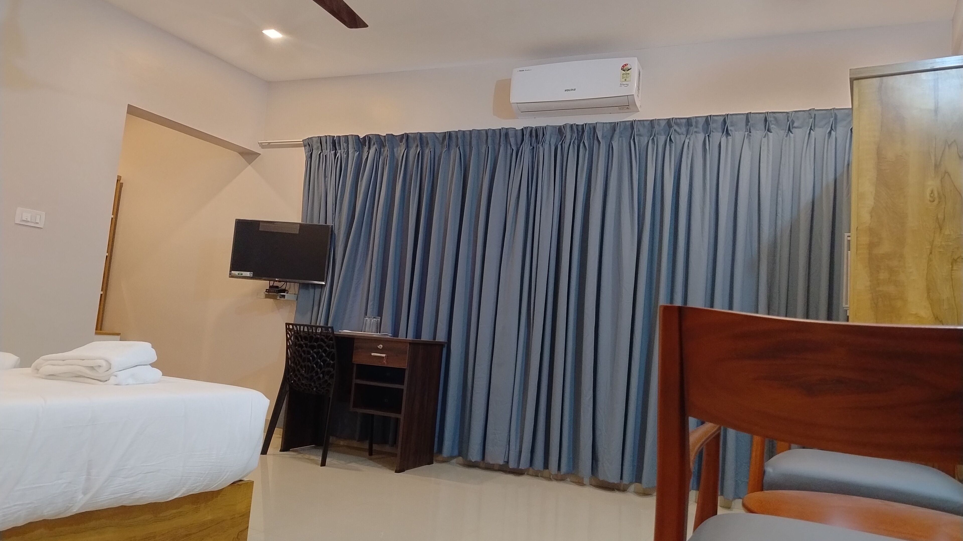 A hotel room with a bed, a desk with a chair, a television, and a large window with curtains.