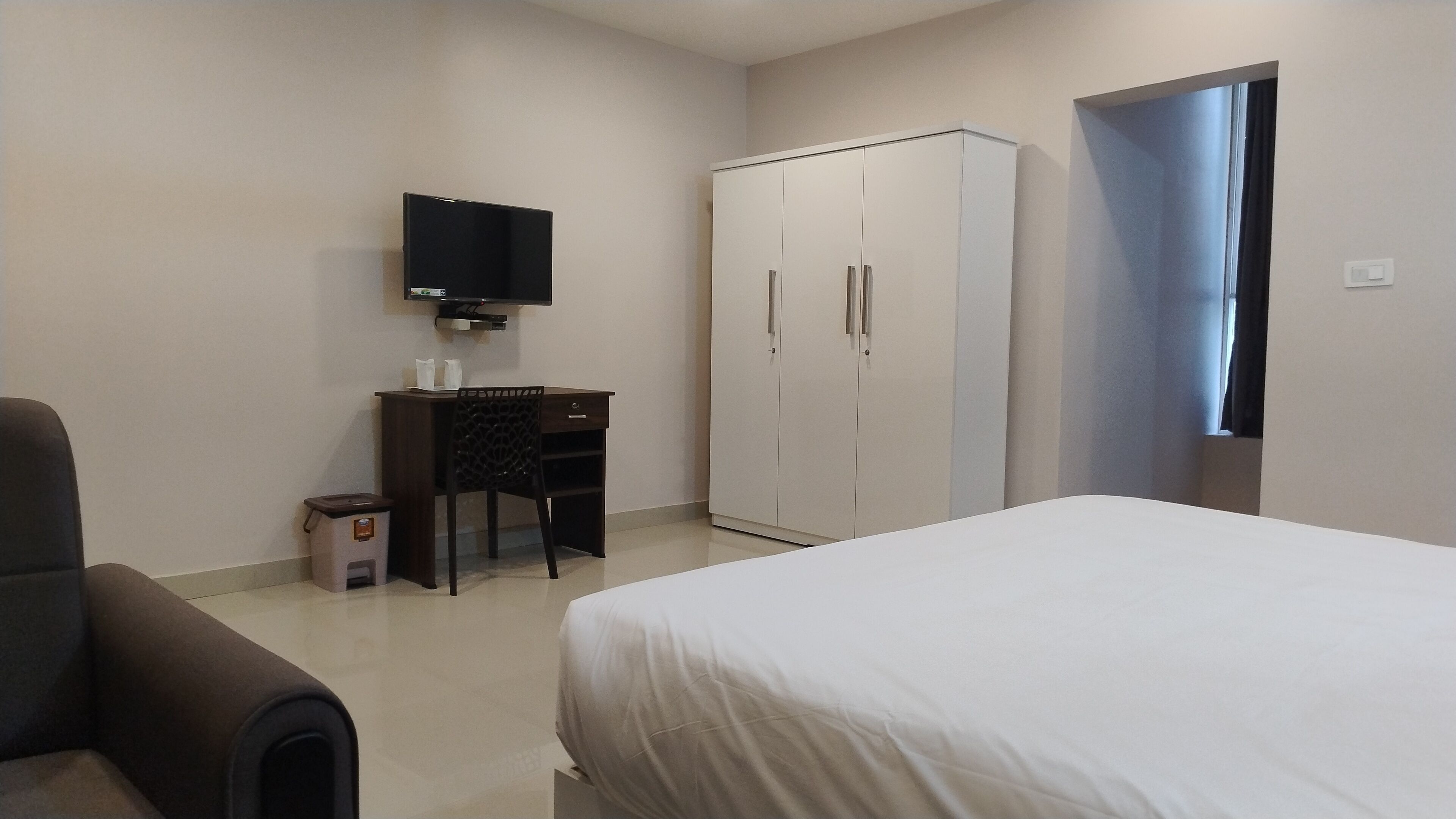 Een hotelkamer met een bed, een bureau met stoel, een kledingkast en een televisie aan de muur.