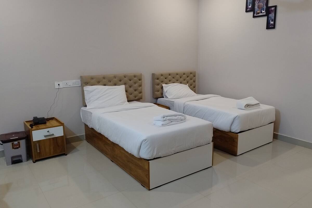 A bedroom with two beds, a nightstand, a drawer unit, and a trash bin.