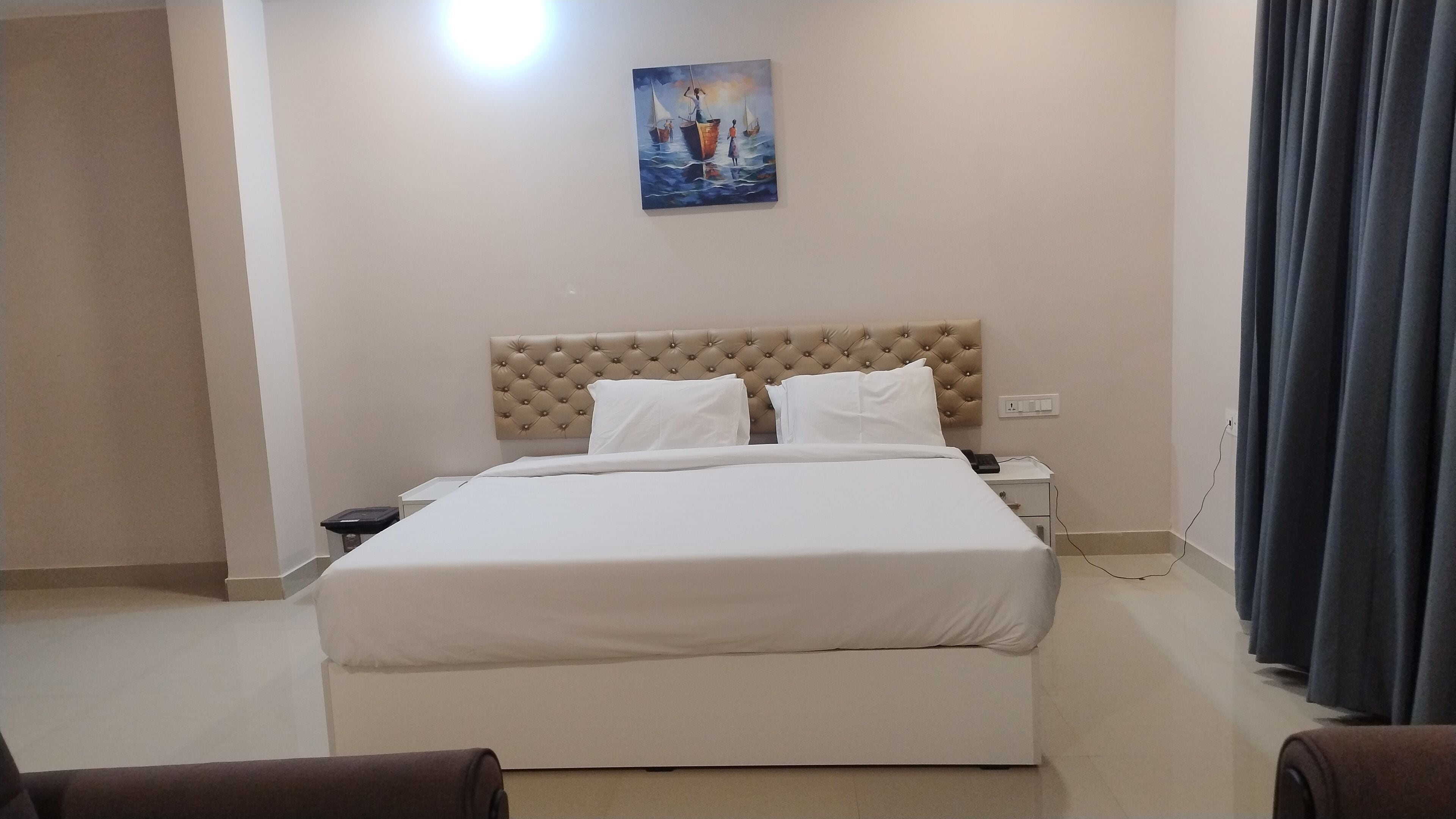Una habitación de hotel con una cama grande, un cabecero, una mesita de noche y un cuadro en la pared.